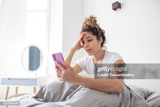 woman in bed reading bad news on her cell phone - dating app stock pictures, royalty-free photos & images
