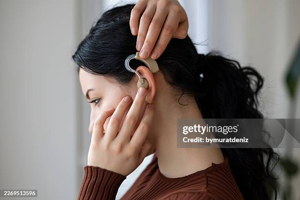 woman putting on digital hearing aid to improve her hearing - inner ear stock pictures, royalty-free photos & images