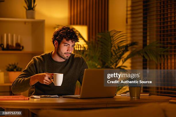 young man working late on laptop at home office with coffee and plants - flexplekken stockfoto's en -beelden