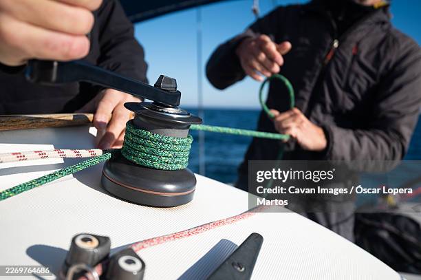 sailors adjusting sailboat rope on a winch during regatta - polea fotografías e imágenes de stock