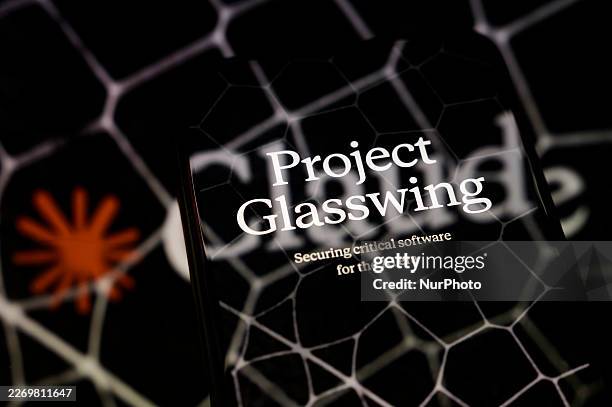 The visual for Project Glasswing is displayed on a smartphone screen placed on a reflective surface onto which a Claude logo with hexagonal patterns...