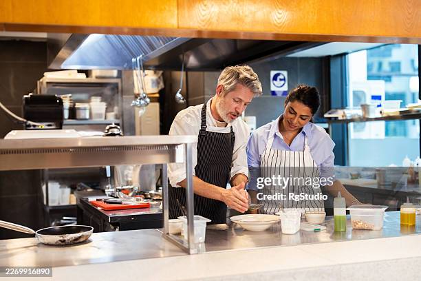 chef teaching apprentice cooking techniques in restaurant kitchen - apprentice chef stock pictures, royalty-free photos & images