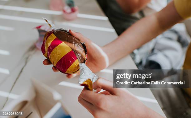 child unwrapping large chocolate easter egg - unwrapping candy stock pictures, royalty-free photos & images