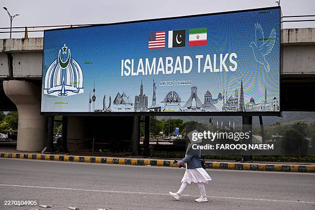 Woman walks past a digital screen displaying news of USIran peace talks along a road in Islamabad on April 10, 2026. A cloud of uncertainty hung...