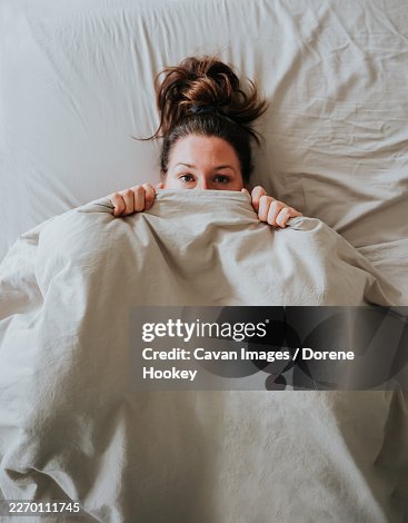 Top view of woman in bed hiding under covers with blanket over face Top view of woman in bed hiding under covers with blanket over face