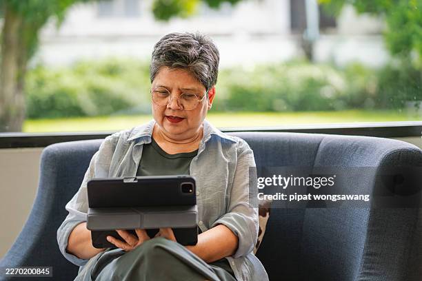 senior woman using tablet while sitting on sofa - screen reader accessibility stock pictures, royalty-free photos & images