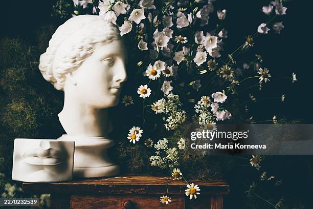 a classical plaster bust and david's lips fragment arranged with wildflowers on a rustic wooden table. - bust sculpture stock pictures, royalty-free photos & images