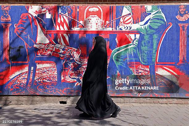 Woman walks past an anti-US mural depicting Iran-US talks near the former US embassy in Tehran on April 11, 2026. An Iranian government delegation...