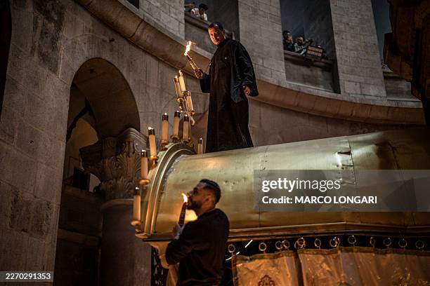 Orthodox Christian priests light candles while standing atop the Edicule, traditionally believed to be the burial site of Jesus Christ, during the...