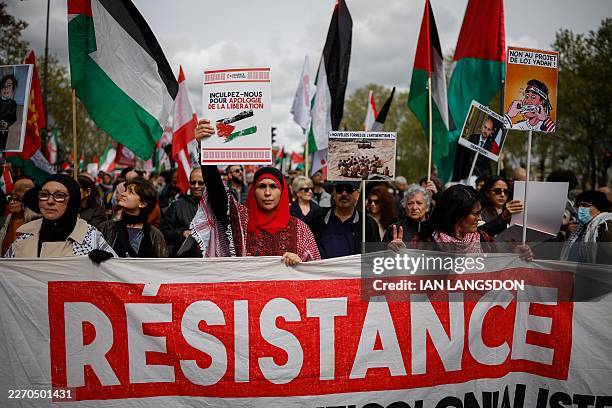 Person holds a placard reading "Charge us for advocating liberation" as protesters hold a banner and Palestinian flags during a rally against the...