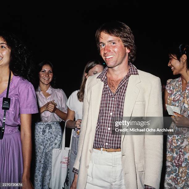 American actor John Ritter, wearing a white blazer over a checked shirt, with several women in the background, United States, circa 1980.