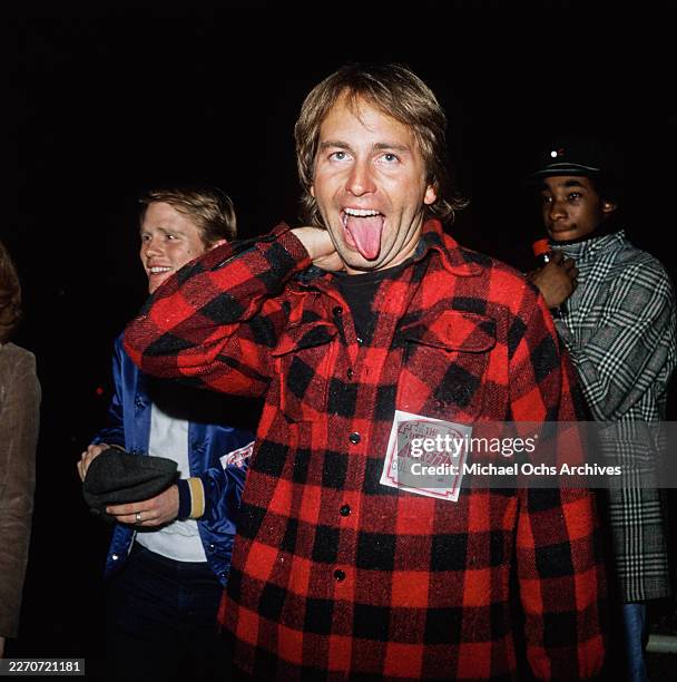 American actor John Ritter, wearing a red-and-black checked shirt, with a 'The Return of Kiss' 'Guest Pass' attached, with American actor and film...