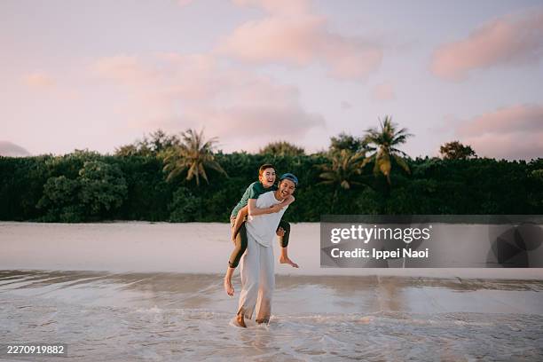 father giving piggyback to daughter on tropical beach at sunset - irabu island foto e immagini stock