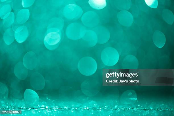a serene christmas ambiance shines through a wintery green haze. the defocused particles float like falling coins in the celebration air. designed for use in holiday backgrounds and festive graphics. - fondo turquesa fotografías e imágenes de stock