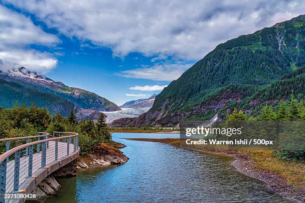 scenic view of a winding river amidst majestic mountains with a glacier under a vibrant sky, featuring a wooden boardwalk in the foreground - alaska stock pictures, royalty-free photos & images