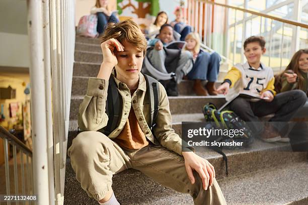 un chico triste siendo acosado por sus amigos en las escaleras de un pasillo. - sonrisa sarcástica fotografías e imágenes de stock