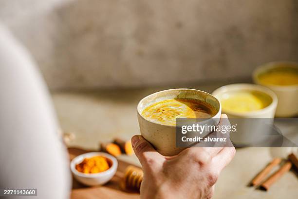hand holding ceramic mug of turmeric latte with spices - turmeric stock pictures, royalty-free photos & images