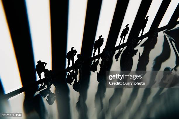 a group of small silhouetted figures stands along a sharp edge against a backdrop of bright vertical stripes of light. - philosophy stock pictures, royalty-free photos & images