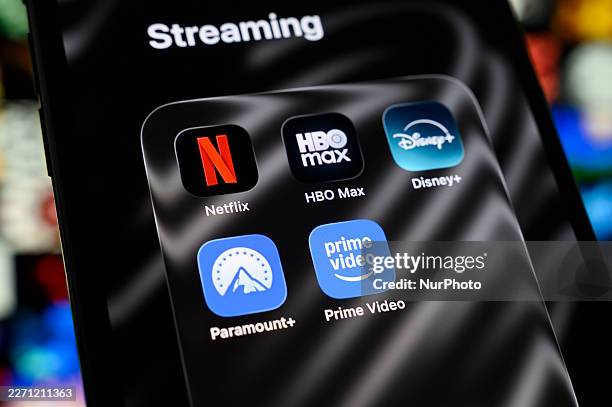 Folder of streaming apps containing Netflix, HBO Max, Disney+, Paramount+, and Prime Video appears on a smartphone screen with a blurred mosaic of...