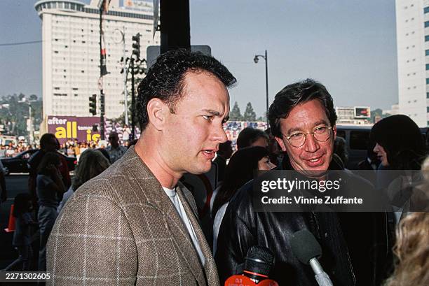 American actor Tom Hanks, wearing a checked brown blazer over a white t-shirt, and American actor and comedian Tim Allen, who wears a black leather...