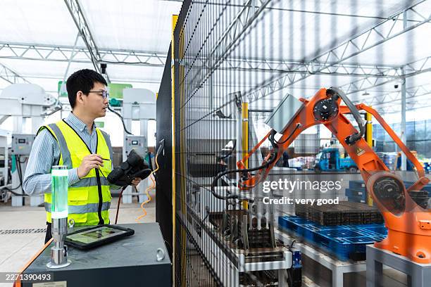 an asian engineer controls a robotic arm using a tablet. - robotic machine stock pictures, royalty-free photos & images