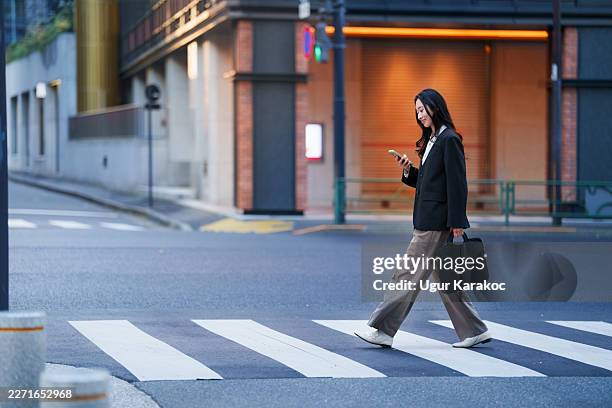 japanese businesswoman looking at smartphone while crossing city street - crossing stock pictures, royalty-free photos & images