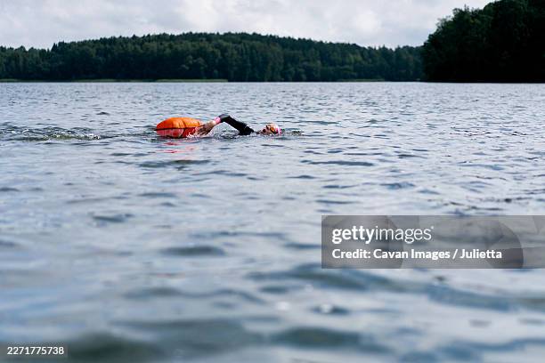 woman in wetsuit with buoy swimming across lake, open water training - boje stock-fotos und bilder