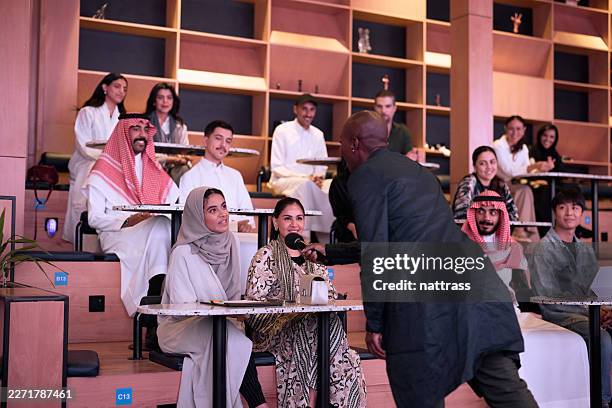 multicultural audience engages with speaker during interactive lecture in modern tiered classroom - saudi classroom stock pictures, royalty-free photos & images