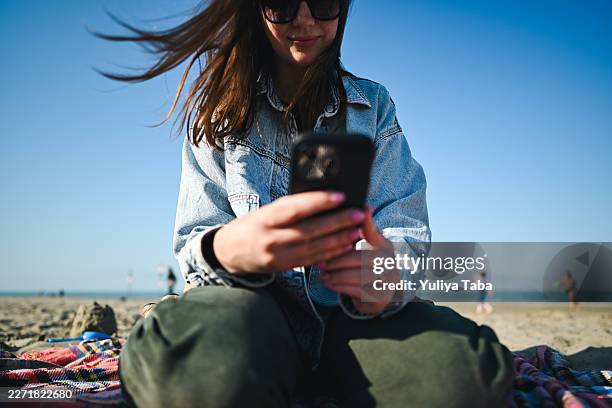 woman texting on smartphone at sunny beach - shallow ai stock pictures, royalty-free photos & images