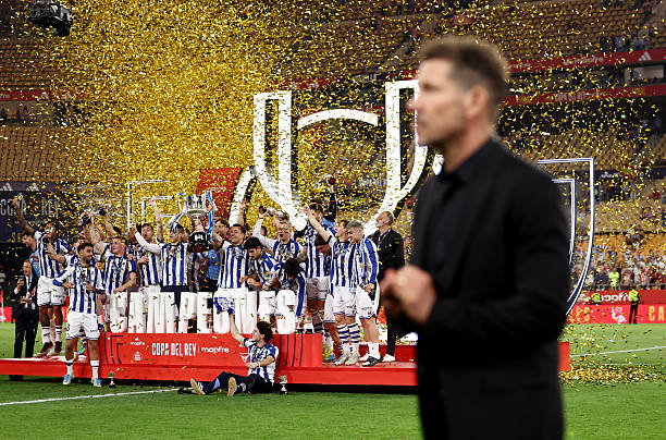 Diego Simeone, Head Coach of Atletico de Madrid, walks in front of the podium as Mikel Oyarzabal of Real Sociedad lifts the Copa Del Rey trophy...
