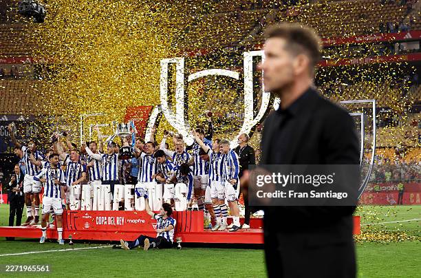 Diego Simeone, Head Coach of Atletico de Madrid, walks in front of the podium as Mikel Oyarzabal of Real Sociedad lifts the Copa Del Rey trophy...