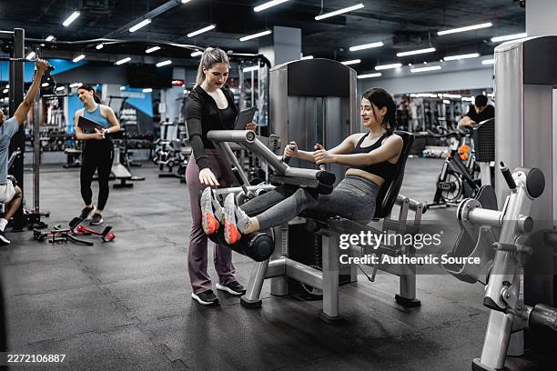 female personal trainer assisting woman on leg extension machine in modern gym - exercise machine stock pictures, royalty-free photos & images