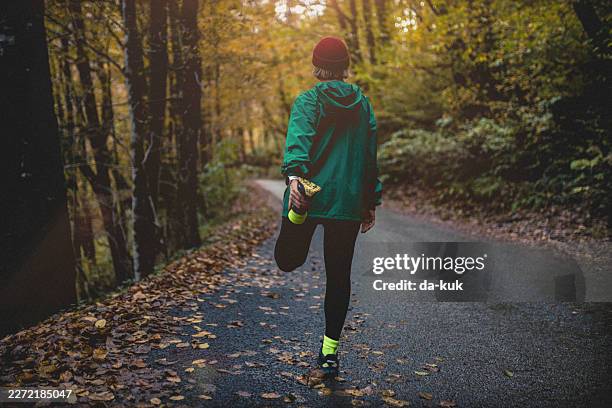 runner stretching on forest trail in autumn jacket preparing for outdoor fitness run - warm clothing stock pictures, royalty-free photos & images