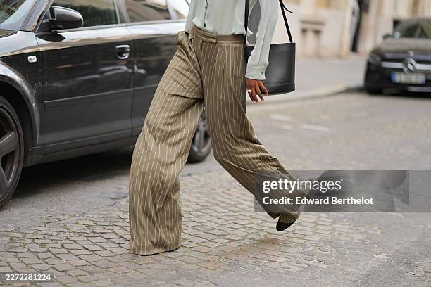 Model wears khaki striped wide leg flared flowing / palazzo pants, black leather pointed shoes, during a street style fashion photo session, outside...