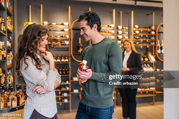 young couple looking at whiskey bottles in a liquor store - whiskey tasting stock pictures, royalty-free photos & images