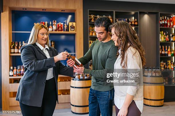 saleswoman helping a young couple in choosing a whiskey bottle in a liquor store - whiskey tasting stock pictures, royalty-free photos & images