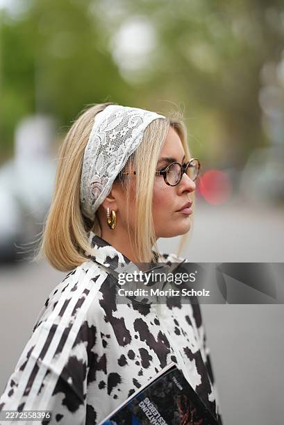 Julia Kammerer is seen wearing a white and brown cow print satin zip up track jacket with a high collar, white ribbed cuffs, a three white side...