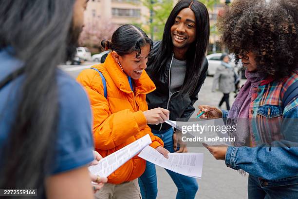 group of students looking at papers and documents together outdoors - petition stock pictures, royalty-free photos & images