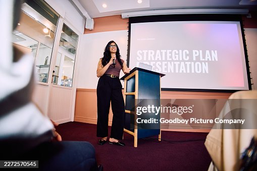 Niedrige Perspektivansicht einer professionellen Frau, die neben dem Rednerpult im Innenraum strategische Planpräsentation hält Niedrige Perspektivansicht einer professionellen Frau, die neben dem Rednerpult im Innenraum strategische Planpräsentation hält