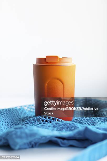 an eco-friendly orange thermo cup prominently placed on textured blue netting, symbolizing sustainability and modern lifestyle - thermo becher stock-fotos und bilder