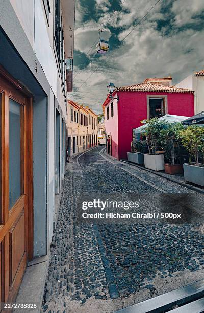 empty cobblestone alleyway winding through colorful buildings with a cable car overhead,portugal - funchal photos et images de collection