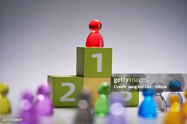 red pawn figure stands on the number one block of a winners podium, surrounded by other colorful pawn figures, symbolizing success and competition - number 2 stock pictures, royalty-free photos & images