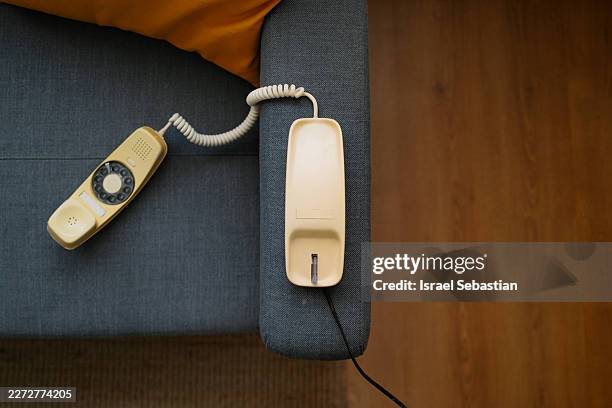 beige rotary telephone with coiled cord rests on gray sofa - teléfono con cable fotografías e imágenes de stock