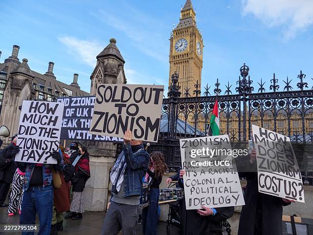 Anti-Zionists holding signs pushing the antisemitic conspiracy about Jewish power at a protest outside the Houses of Parliament, London, UK.