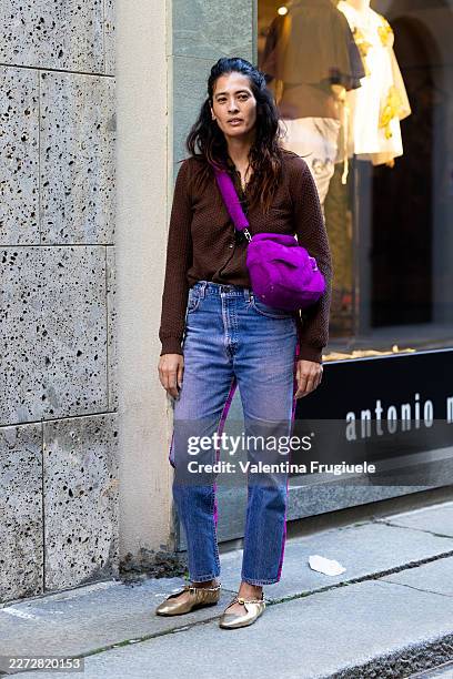 Passerby wears a dark brown textured knit cardigan, light wash straight-leg jeans with purple velvet side stripe detail, a bright magenta fuzzy...