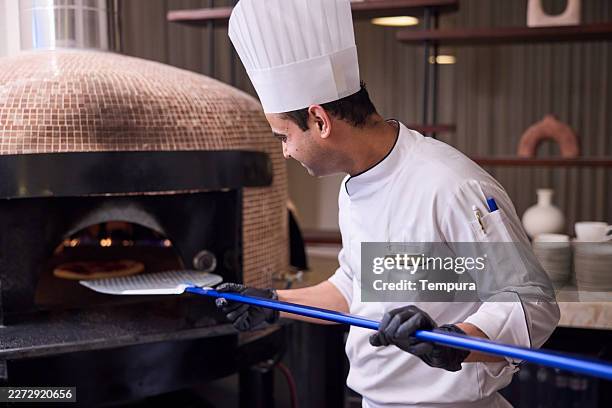 restaurant pizza chef. pizzaiolo is placing a pizza in the oven. - pizza chef stock pictures, royalty-free photos & images