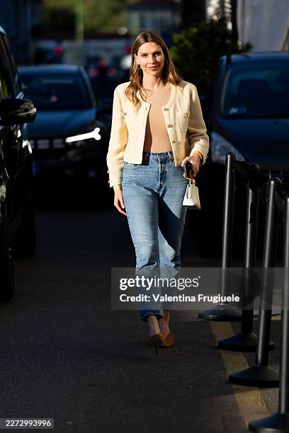 Passerby wears a cream boucle jacket with gold buttons and patch pockets over a nude scoop-neck top, with straight-leg mid-wash blue jeans cropped at...