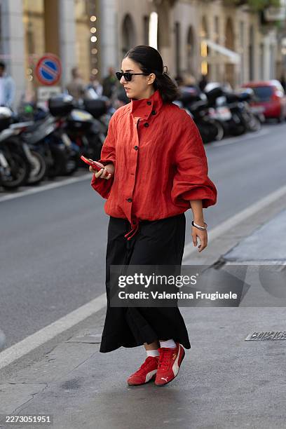 Passerby wears a red oversized linen drawstring-hem jacket over a black maxi skirt, paired with red and white Puma suede sneakers; a silver bangle...