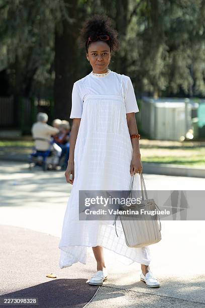 Passerby wears a white embroidered linen pinafore midi dress layered over a white short-sleeve t-shirt, paired with white leather penny loafers,...