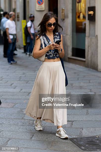 Passerby wears a navy and white paisley-print sleeveless crop top over a beige pleated maxi skirt, paired with gold and beige chunky sneakers,...
